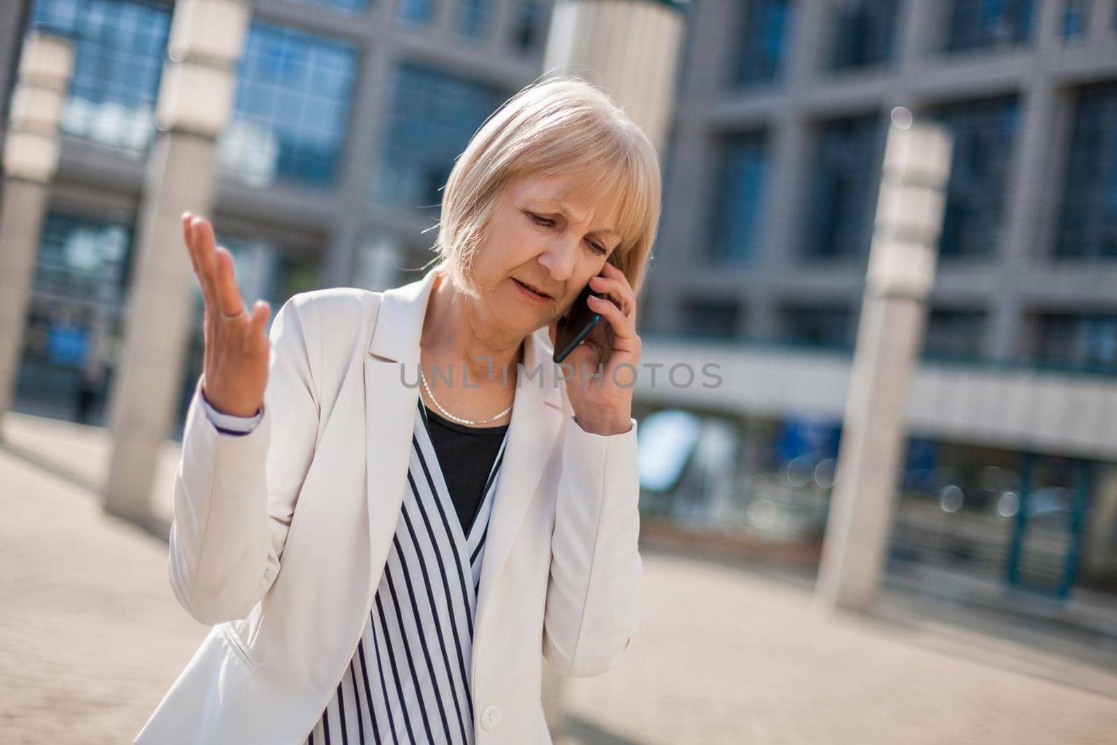 Outdoor portrait of angry senior businesswoman who is talking on phone.