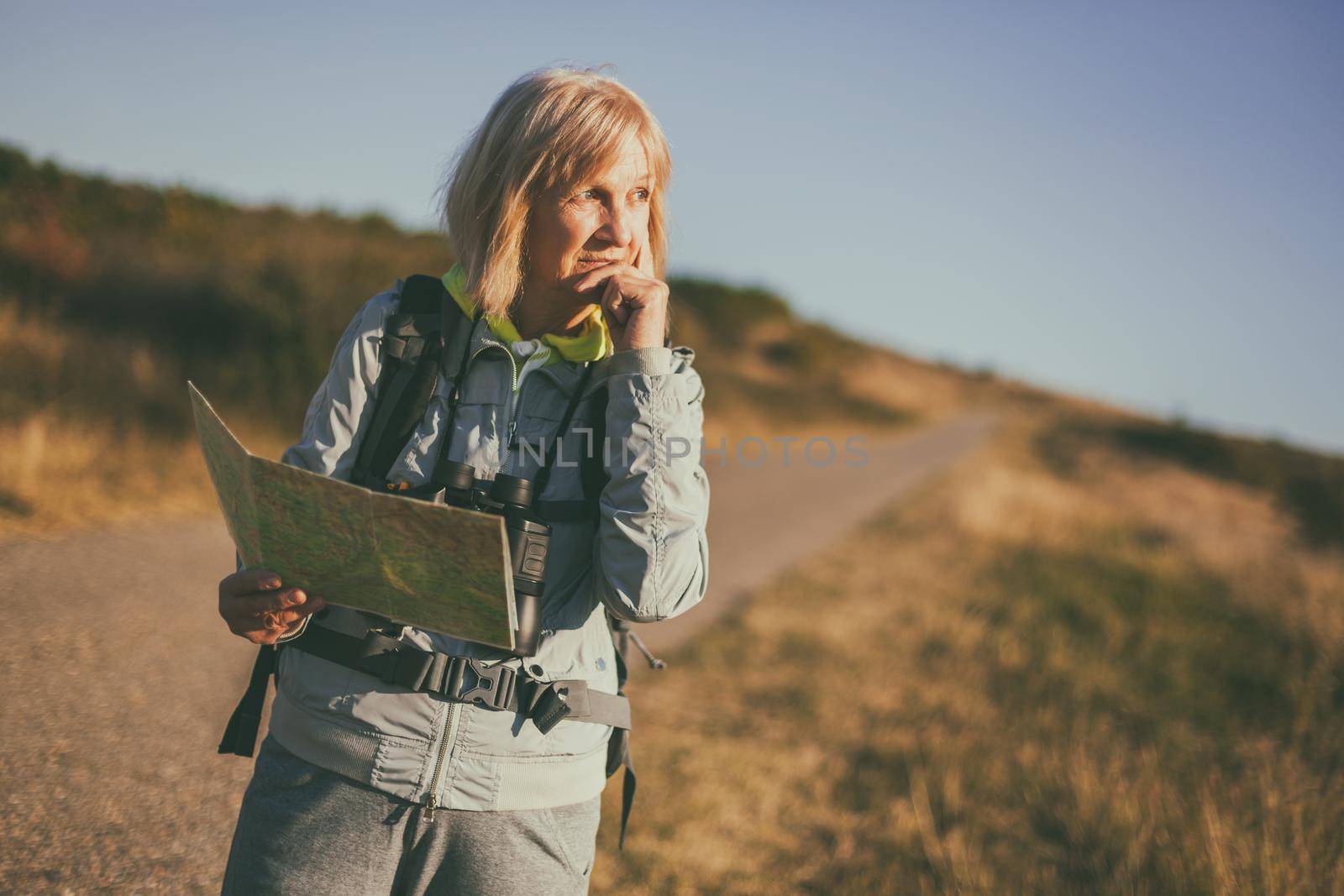 Senior woman is hiking in mountain. Active retirement. She is using map.