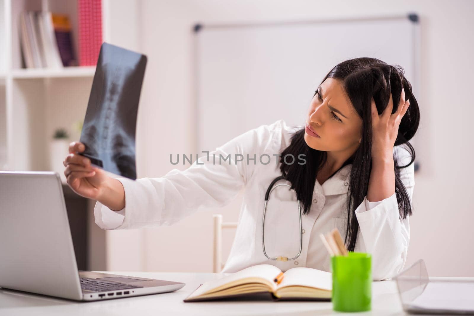 Young doctor is examining x-ray image in her office.