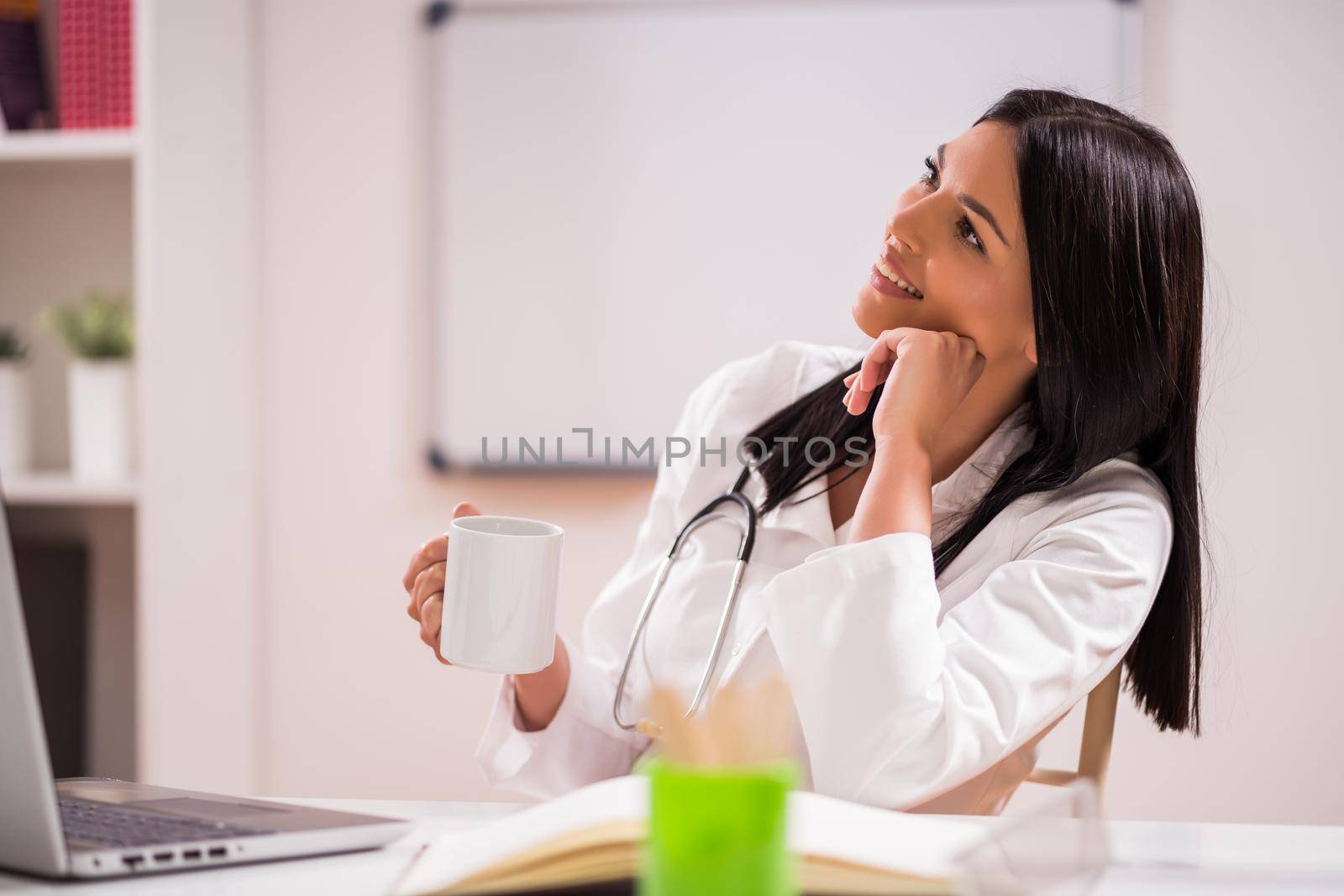 Young doctor is drinking coffee in her office.