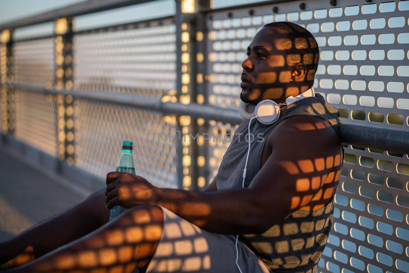 Portrait of young african-american man in sports clothing who is drinking water after jogging.