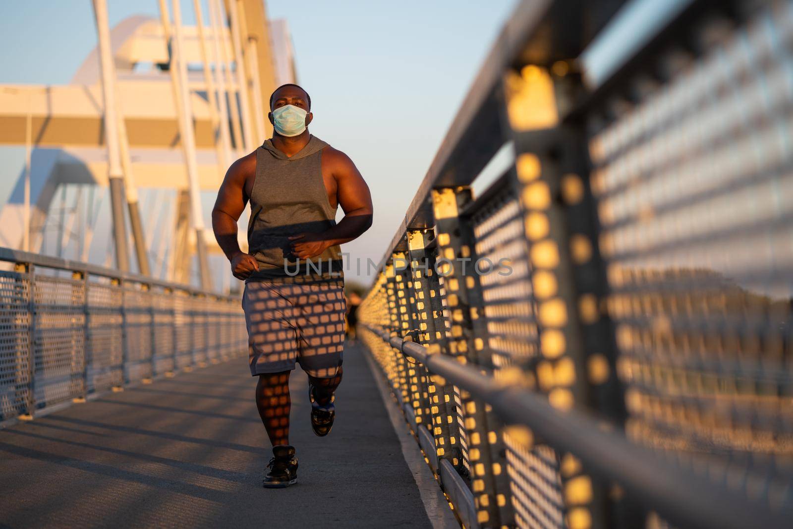 Young african-american man is jogging with protective mask on his face. Corona virus pandemic responsible behavior.