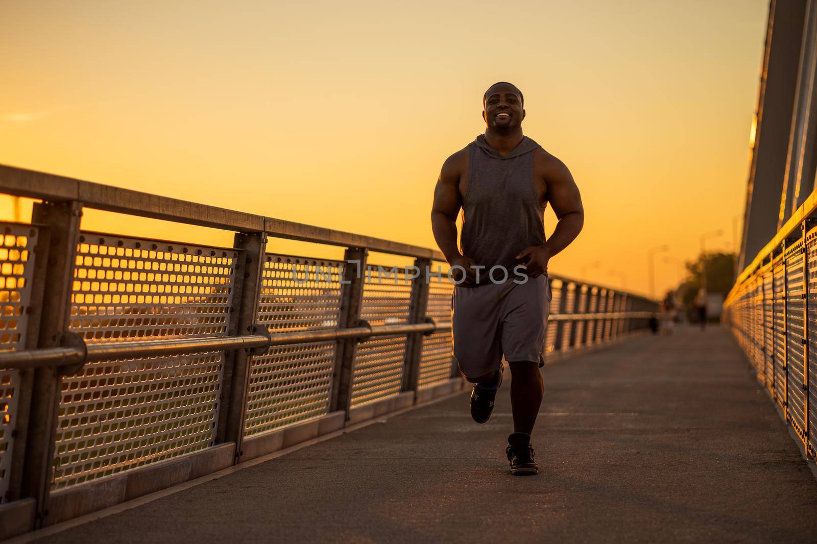 Young african-american man is jogging in sunset on the bridge in the city.