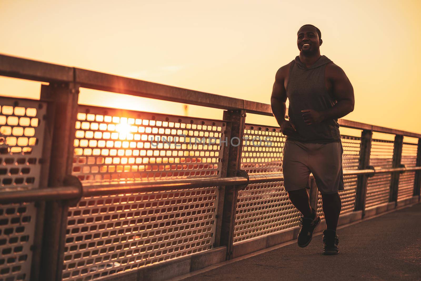 Young african-american man is jogging in sunset on the bridge in the city.