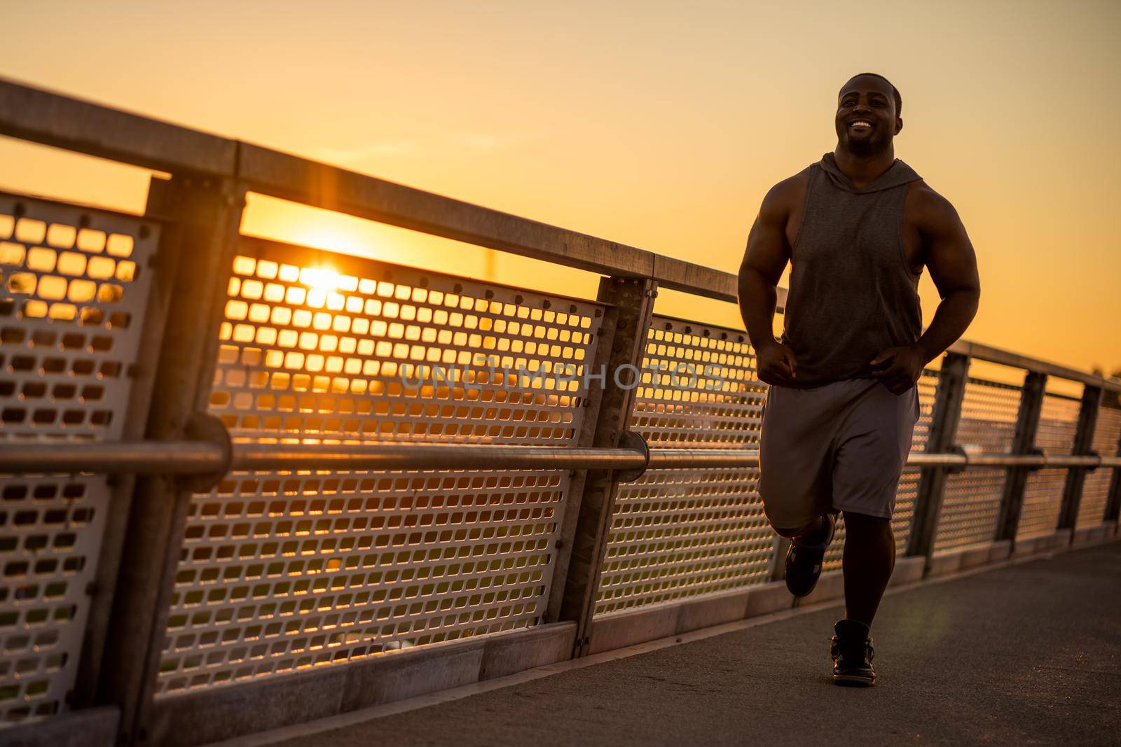 Young african-american man is jogging in sunset on the bridge in the city.