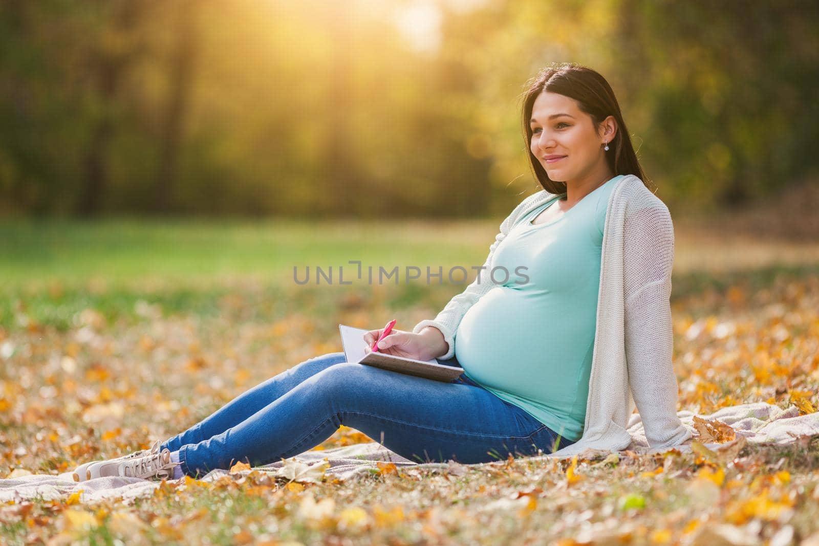 Pregnant woman relaxing in park. She is writing to do list.