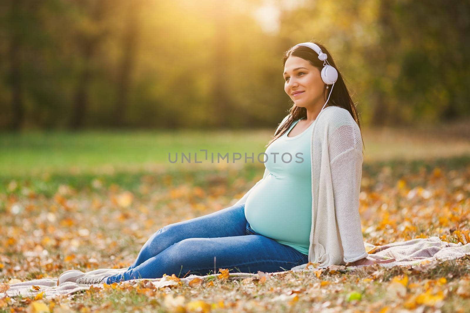 Pregnant woman relaxing in park. She is listening music.