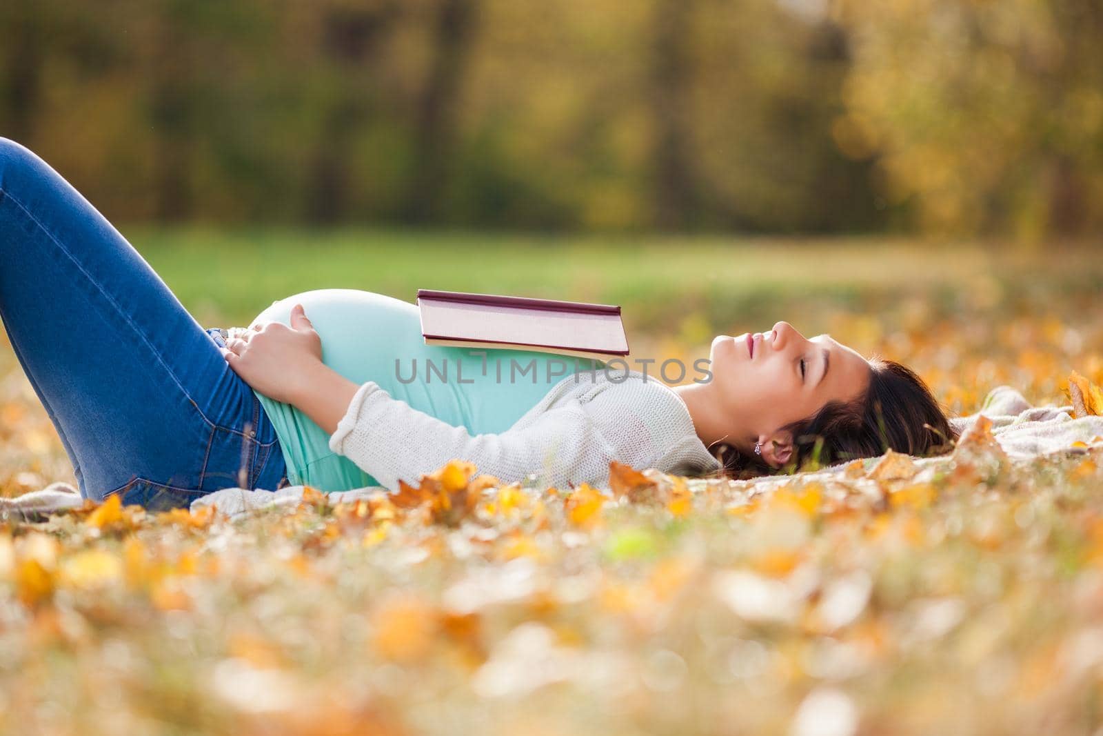 Pregnant woman relaxing in park. She is reading book.