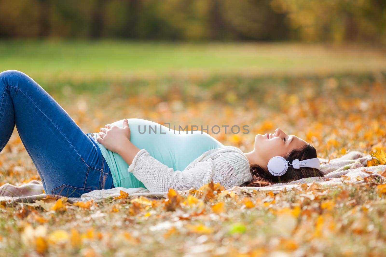 Pregnant woman relaxing in park. She is listening music.