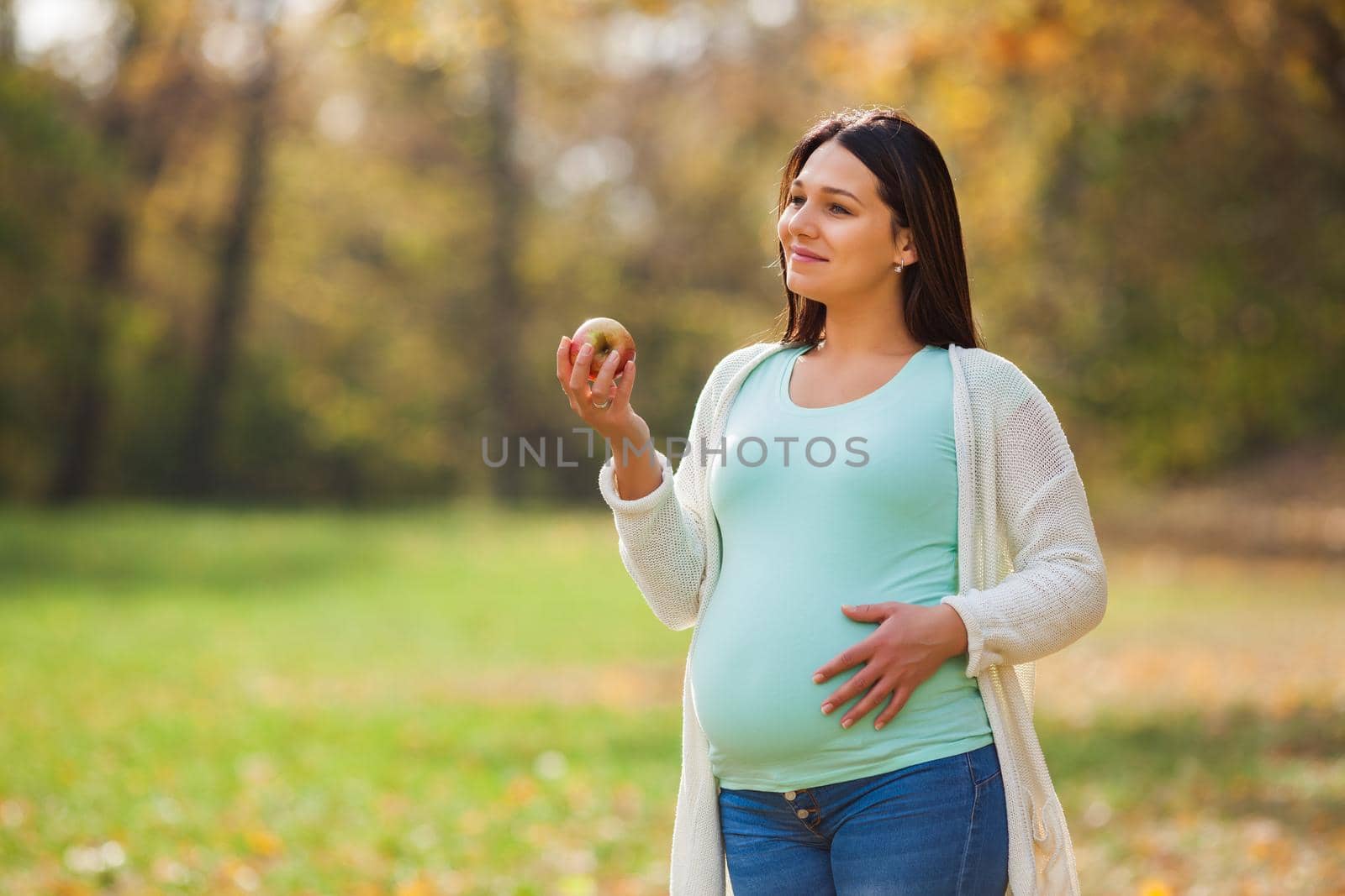 Pregnant woman relaxing in park. She is eating apple.