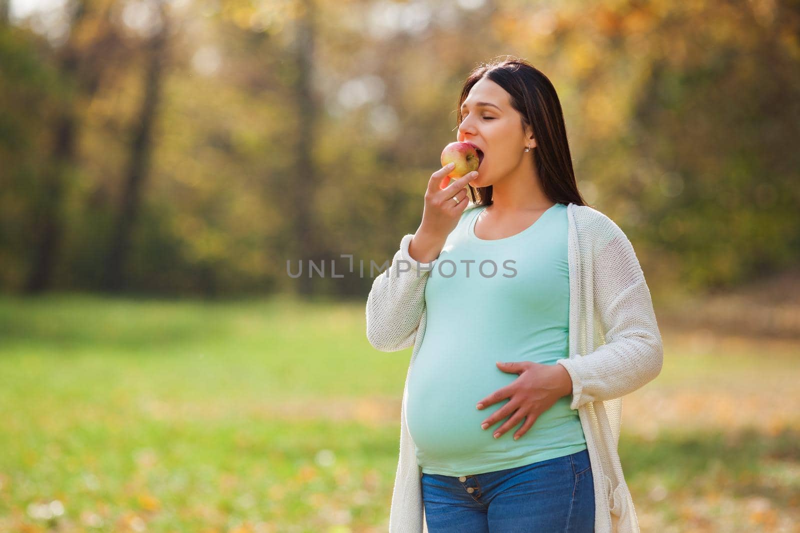 Pregnant woman relaxing in park. She is eating apple.