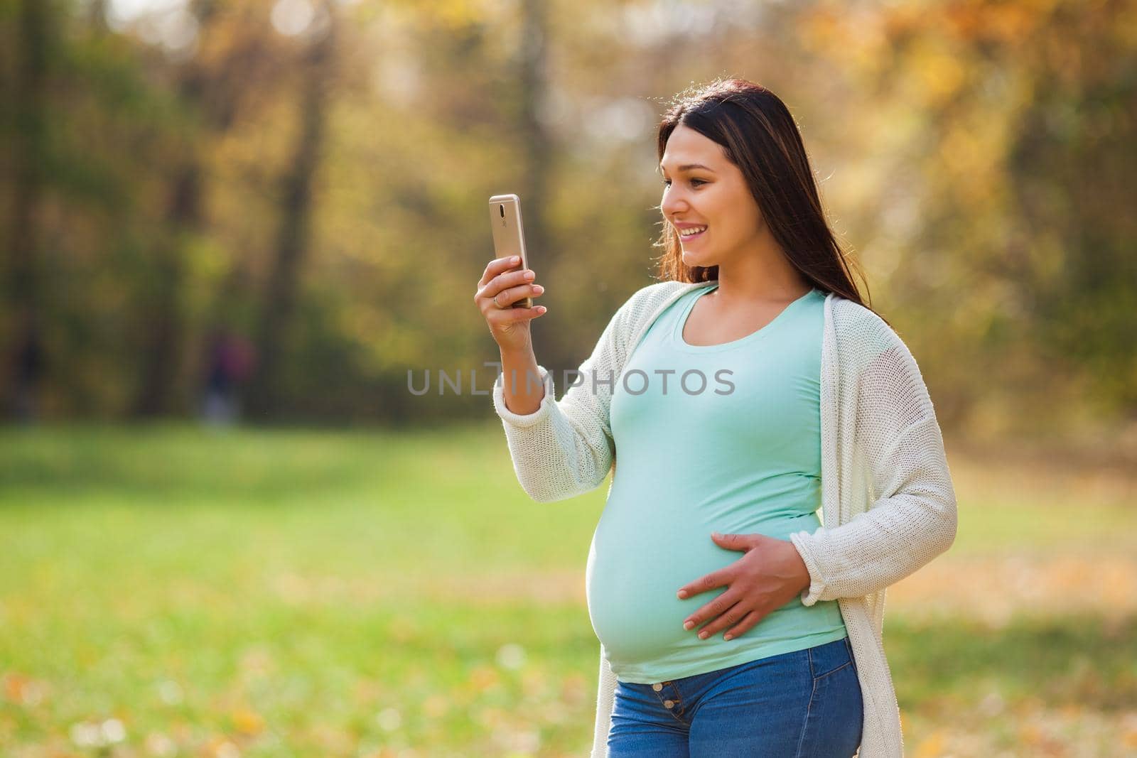 Pregnant woman relaxing in park. She is chatting on smartphone.