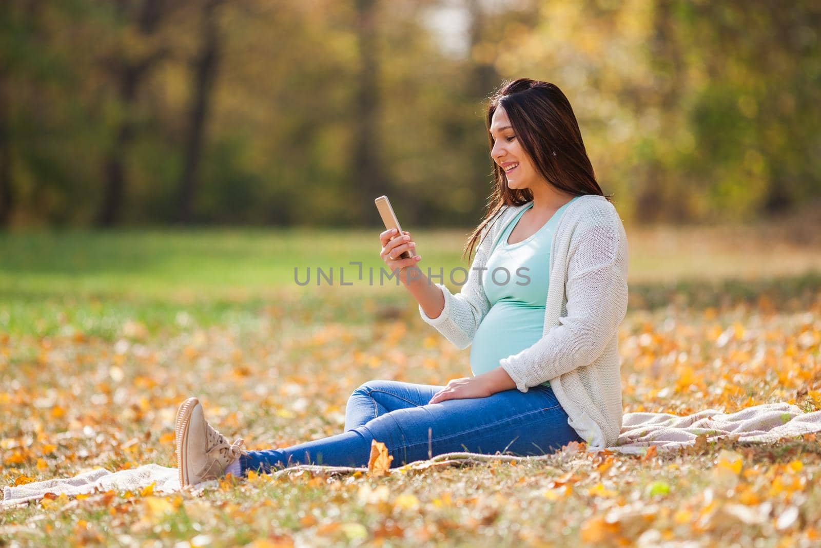 Pregnant woman relaxing in park. She is chatting on smartphone.