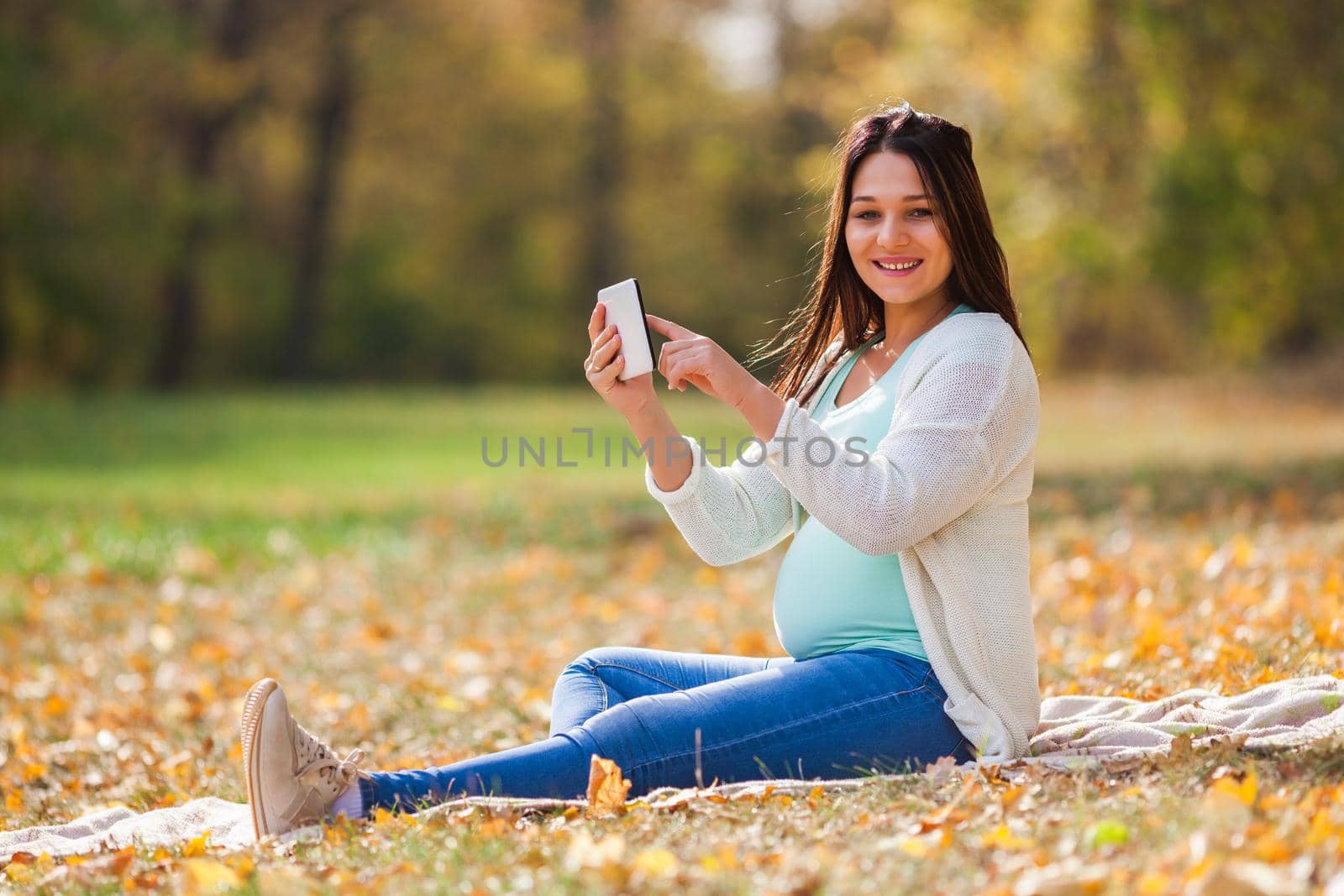 Pregnant woman relaxing in park. She is chatting on digital tablet.