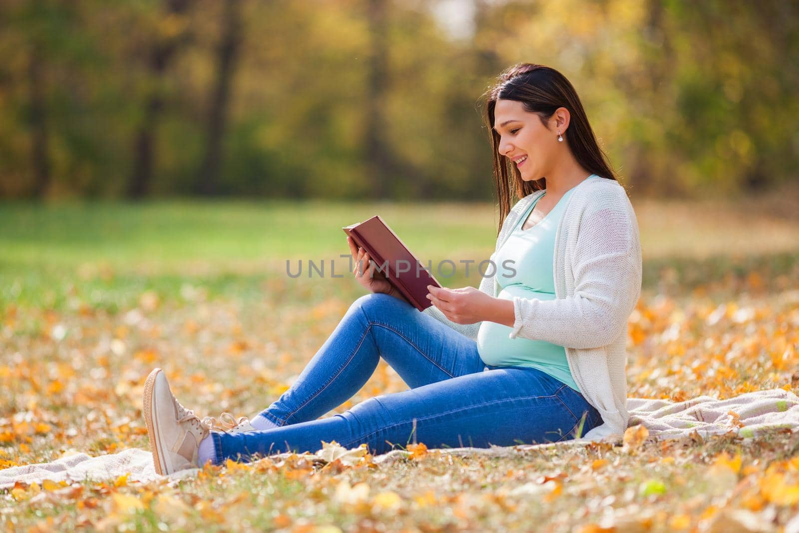 Pregnant woman relaxing in park. She is reading book.