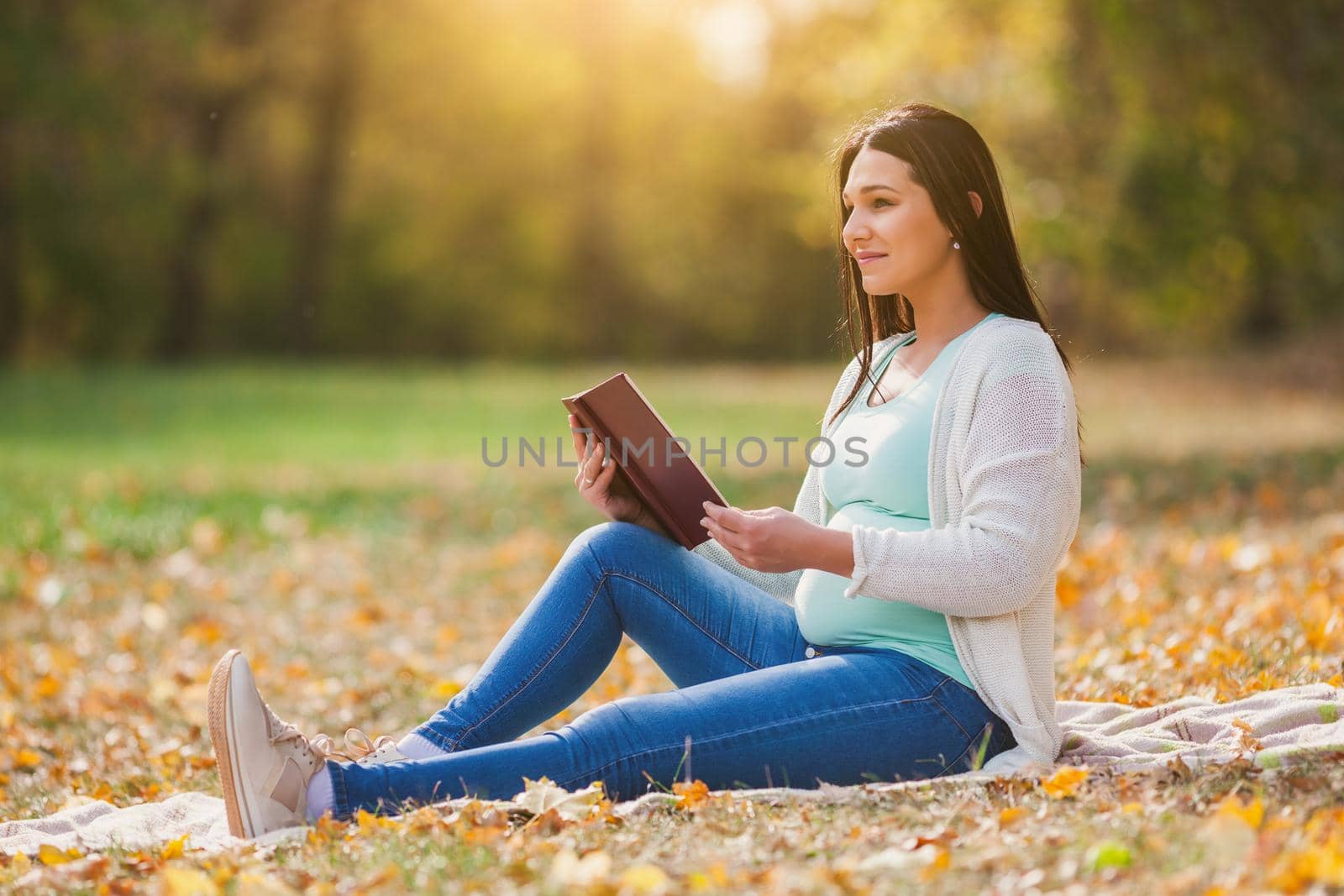 Pregnant woman relaxing in park. She is reading book.