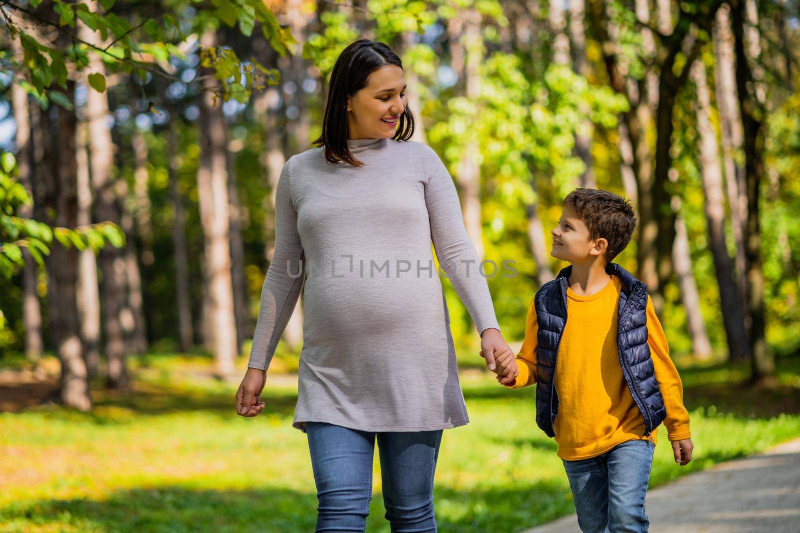 Happy boy and his pregnant mother are enjoying autumn in park.
