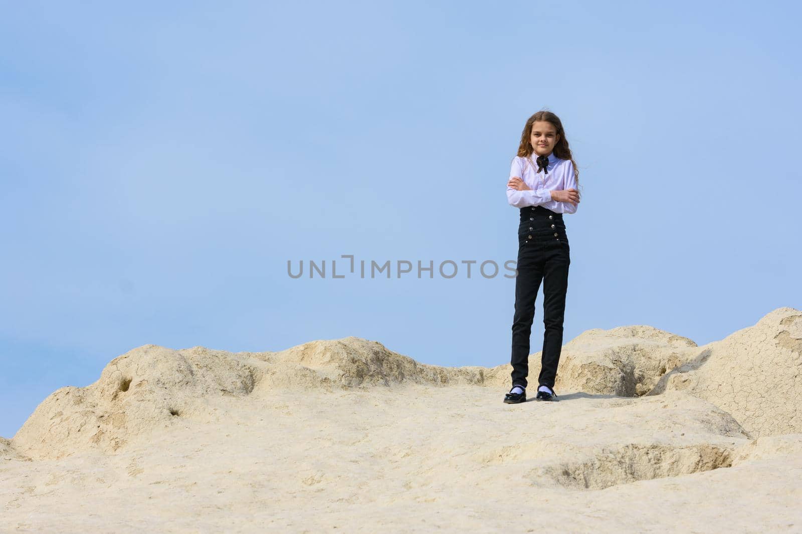 A girl in a white shirt with a bow tie stands on a mountain against the background of the sky