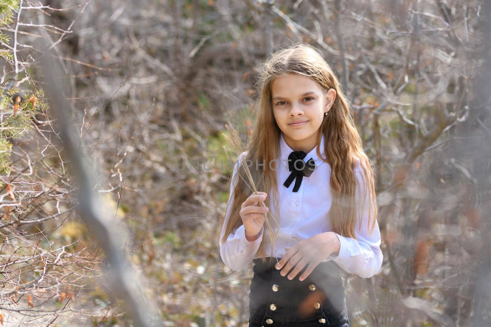 A girl in a white shirt walks through the spring forest and holds several straws in her hands