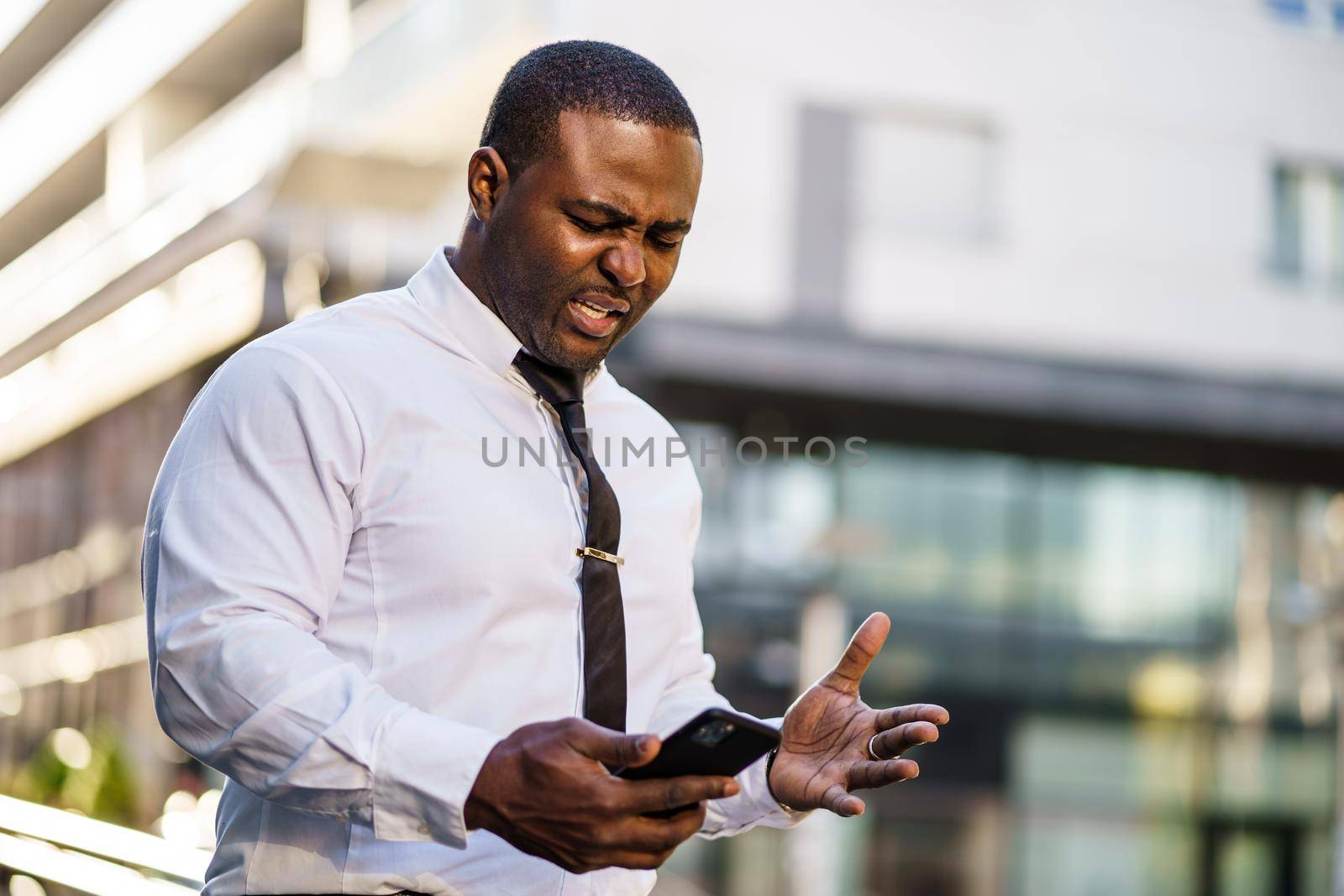 Portrait of frustrated african-american businessman who is using smartphone.
