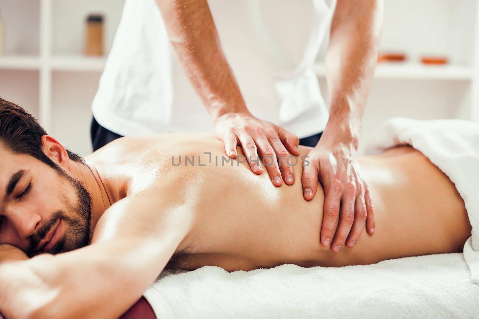 Young man is enjoying massage on spa treatment. Professional masseur is massaging his back.