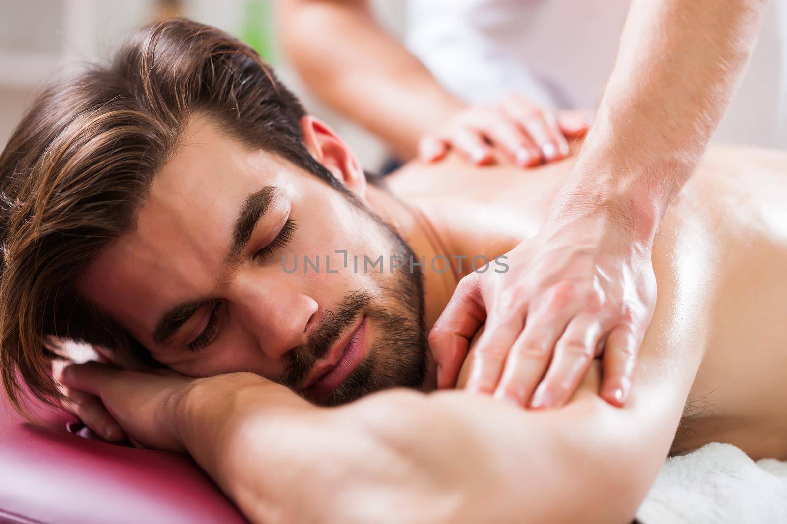 Young man is enjoying massage on spa treatment. Professional masseur massaging back of man.