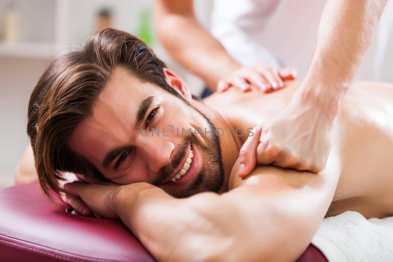 Young man is enjoying massage on spa treatment. Professional masseur massaging back of man.