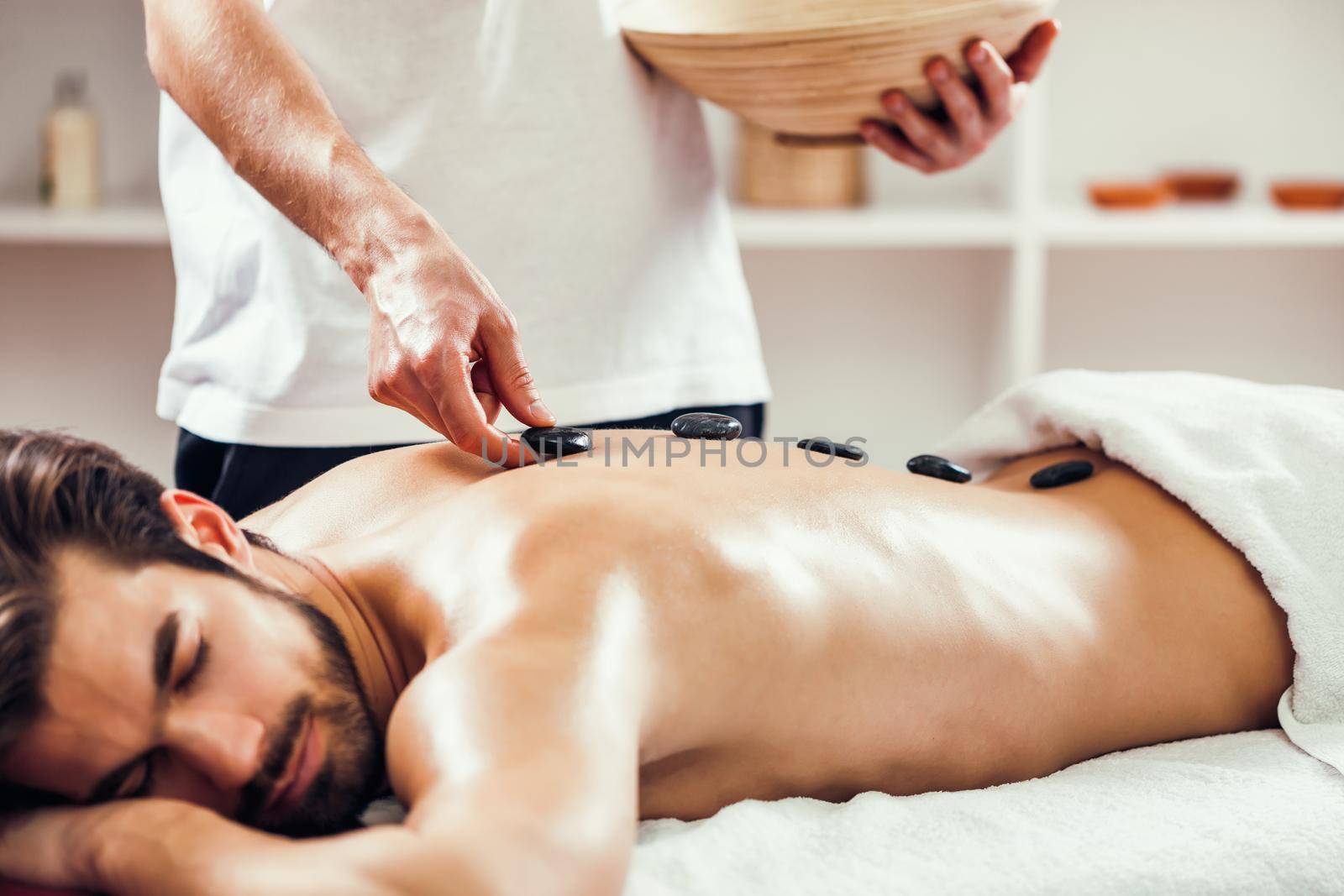 Young man is enjoying hot stone therapy on spa treatment.