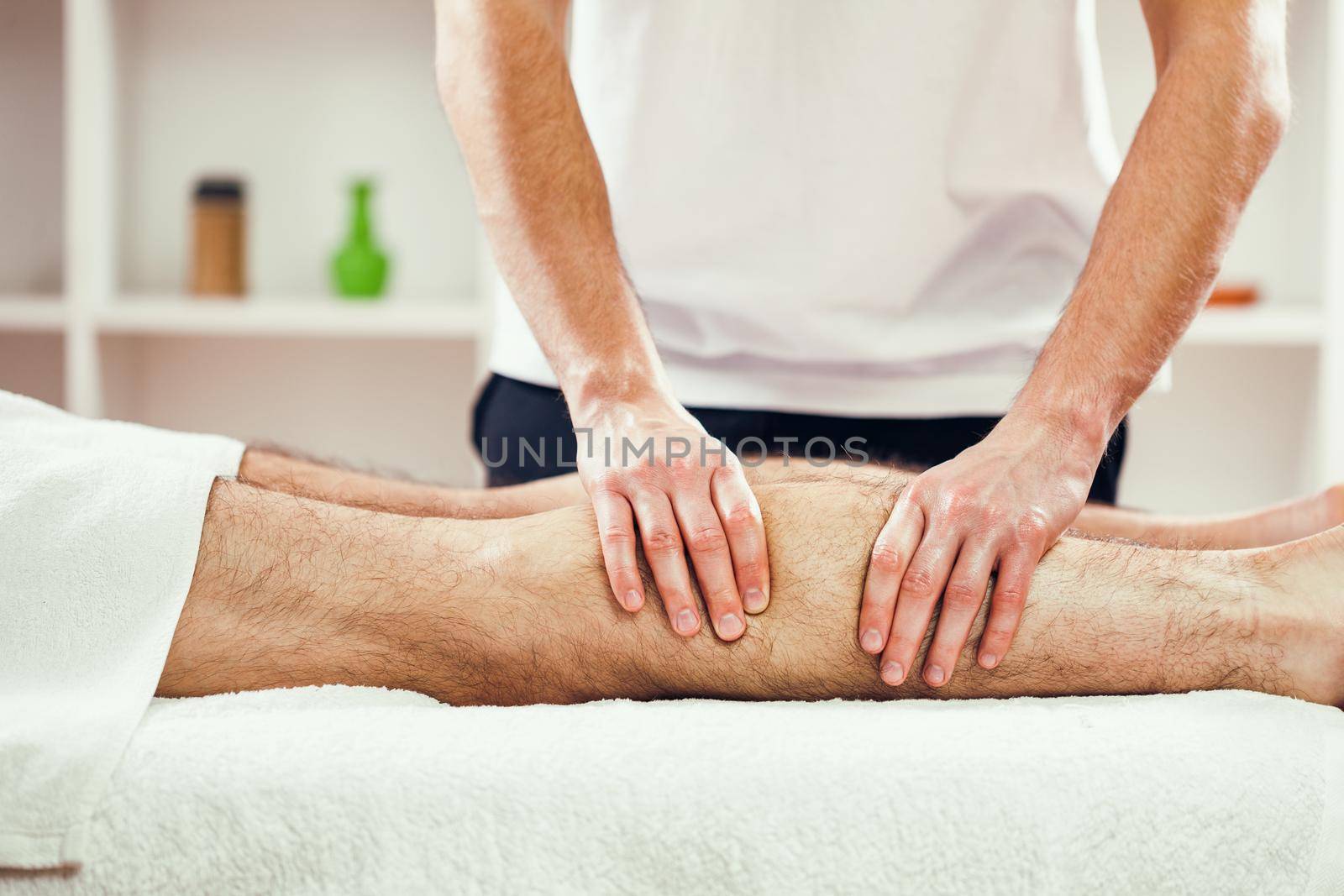 Young man is enjoying massage on spa treatment. Professional masseur is massaging leg of man.