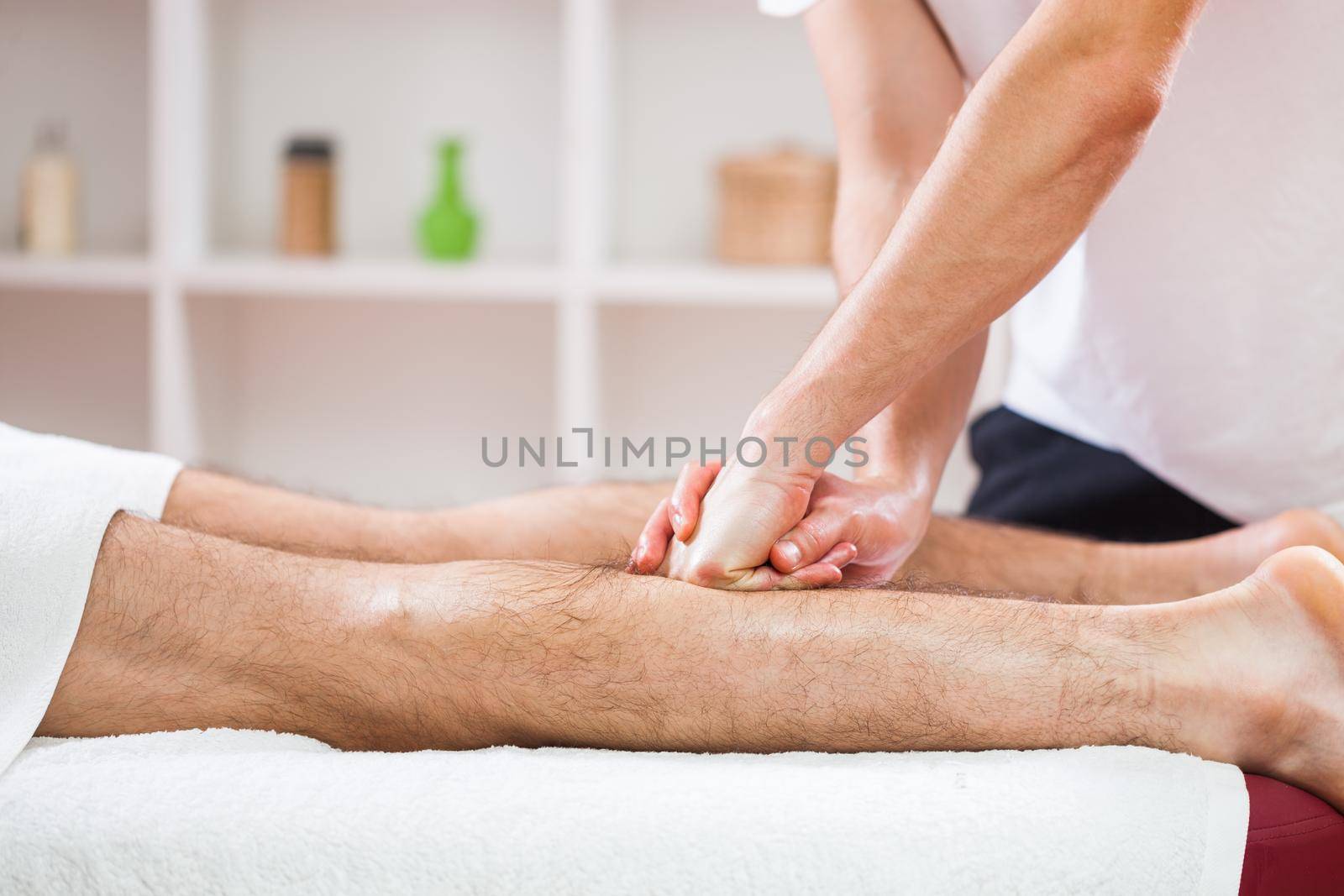 Young man is enjoying massage on spa treatment. Professional masseur is massaging leg of man.