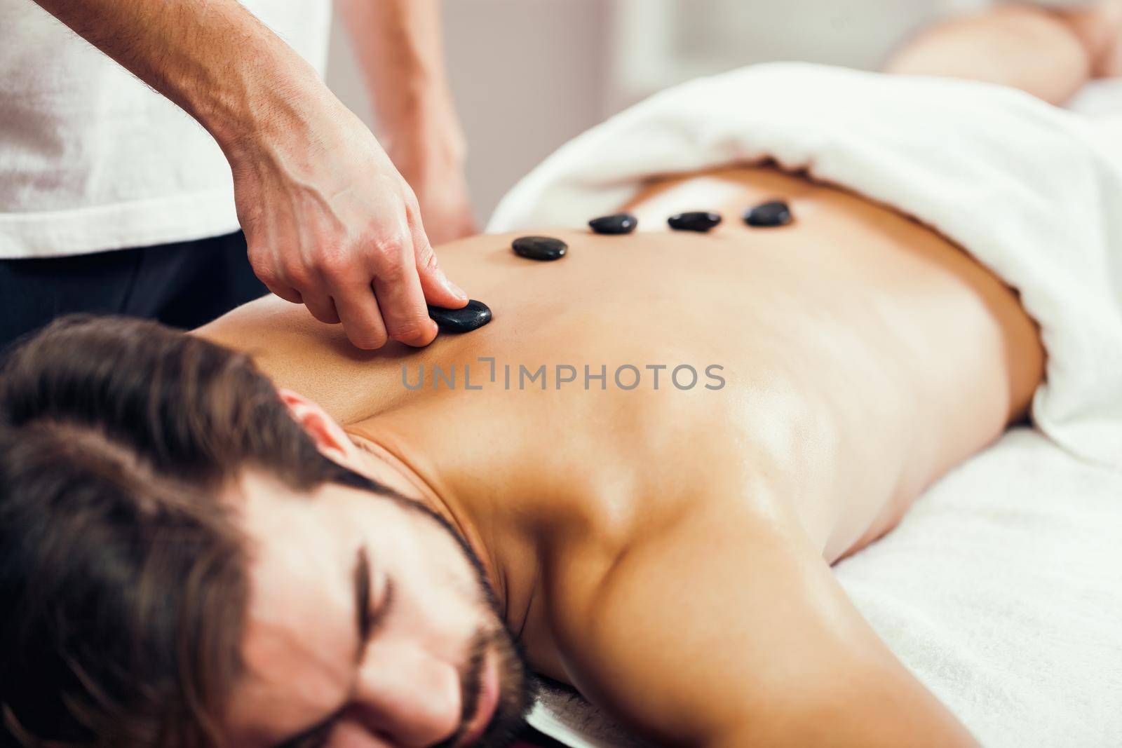 Young man is enjoying hot stone therapy on spa treatment.