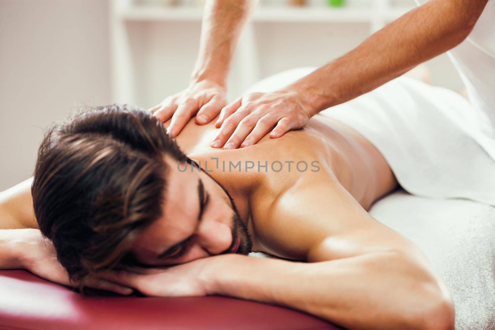 Young man is enjoying massage on spa treatment. Professional masseur massaging back of man.