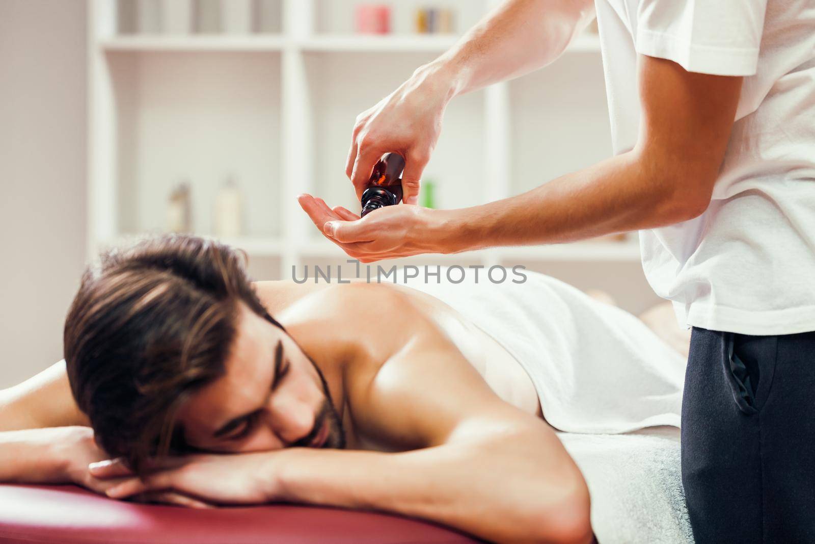 Young man is enjoying massage on spa treatment. Professional masseur is applying massage oil to his skin.