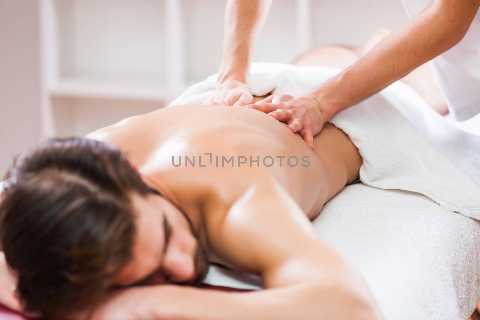 Young man is enjoying massage on spa treatment. Professional masseur massaging back of man.