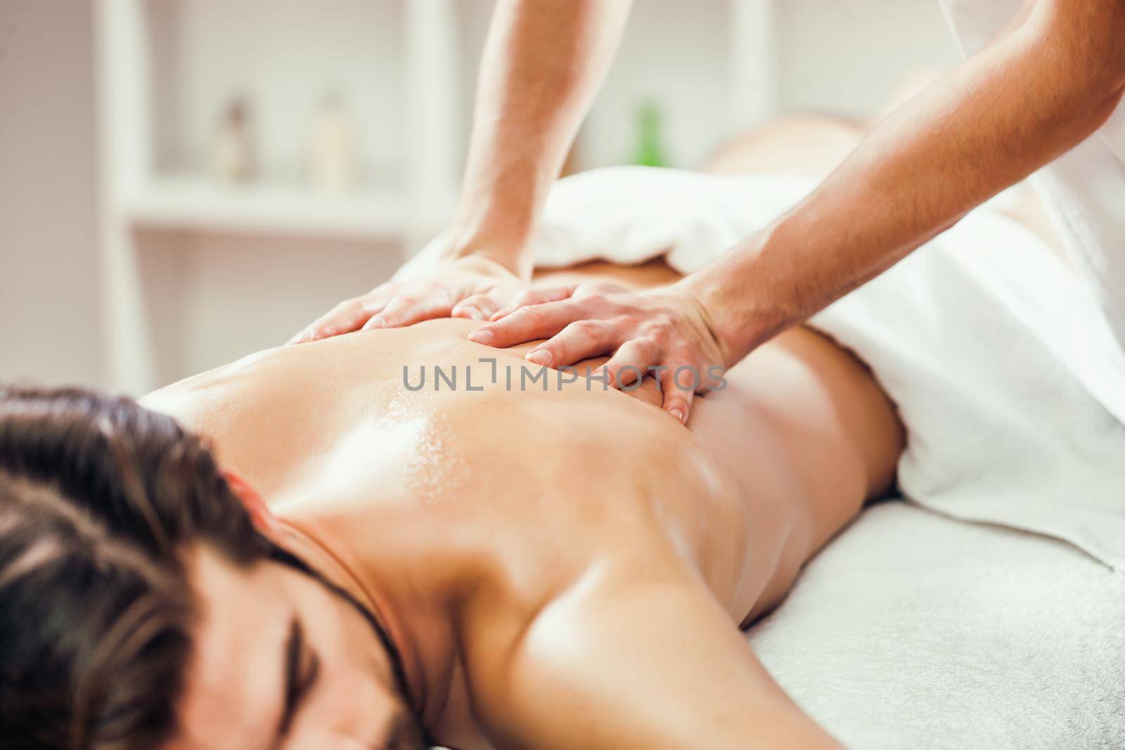 Young man is enjoying massage on spa treatment. Professional masseur massaging back of man.