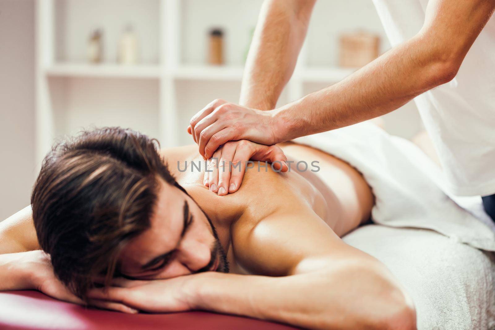 Young man is enjoying massage on spa treatment. Professional masseur massaging back of man.