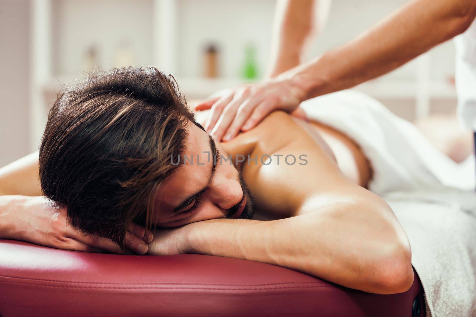 Young man is enjoying massage on spa treatment. Professional masseur massaging back of man.