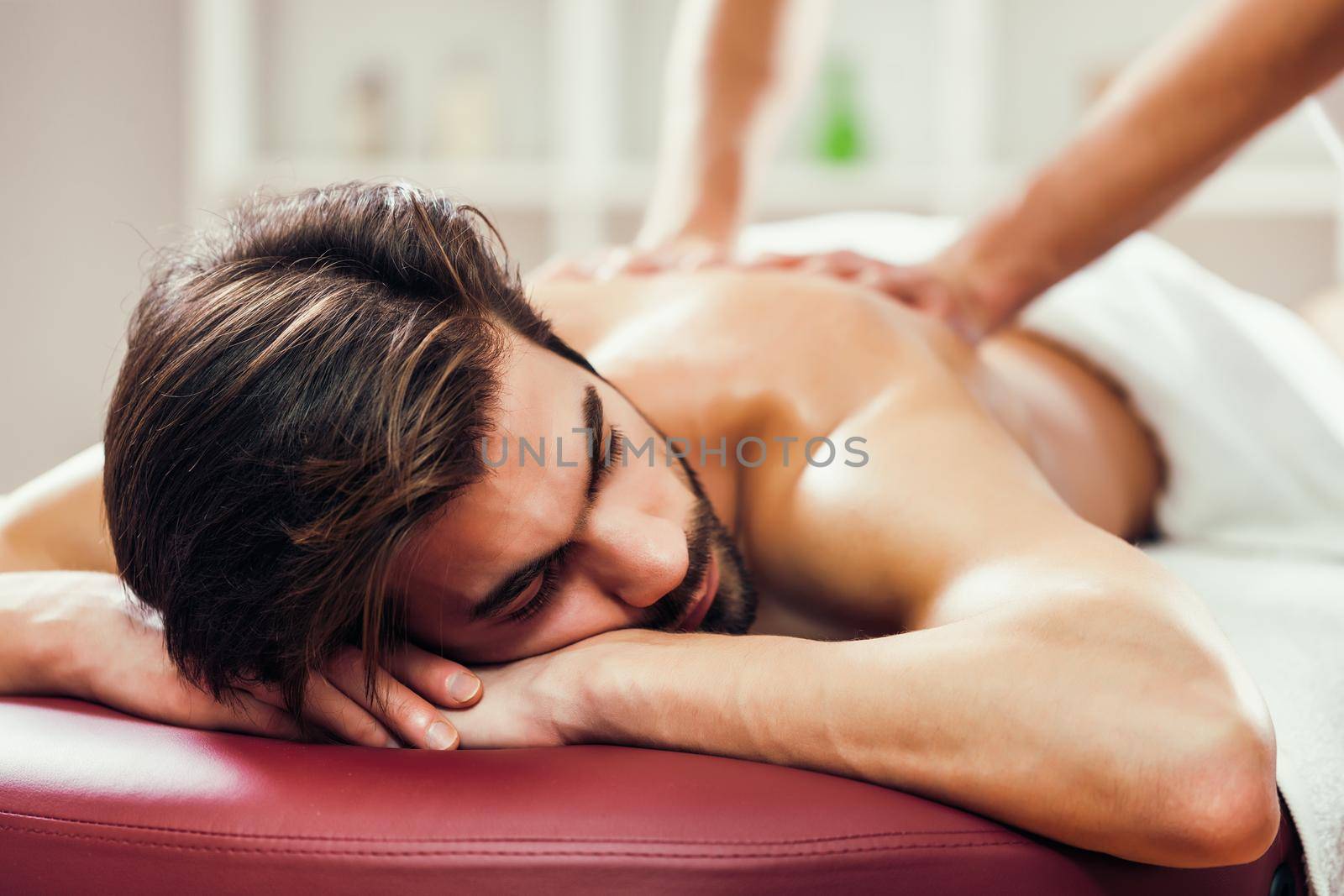 Young man is enjoying massage on spa treatment. Professional masseur massaging back of man.