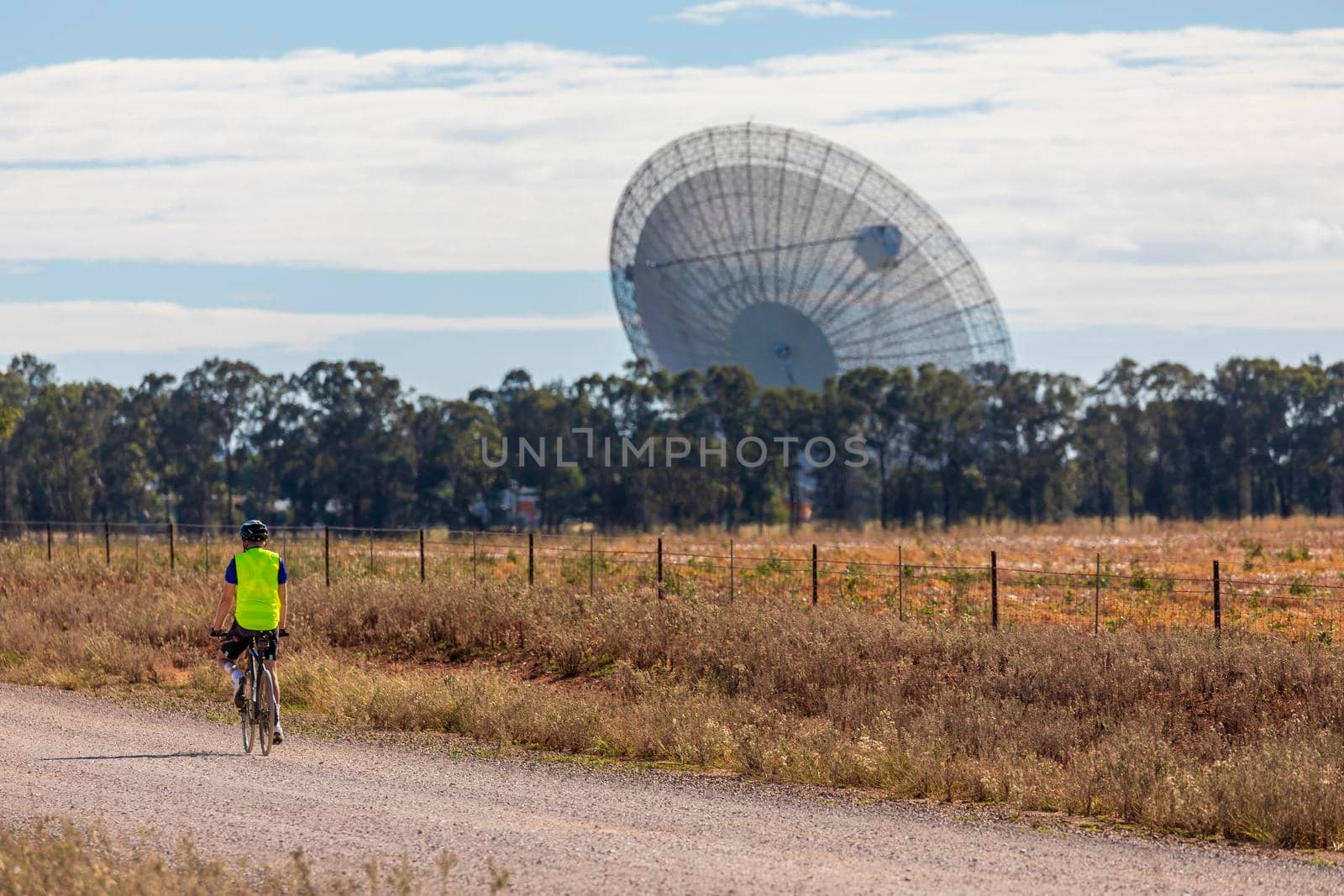 A bicycle rider on a dirt road approaching a large outdoor scientific radio telescope