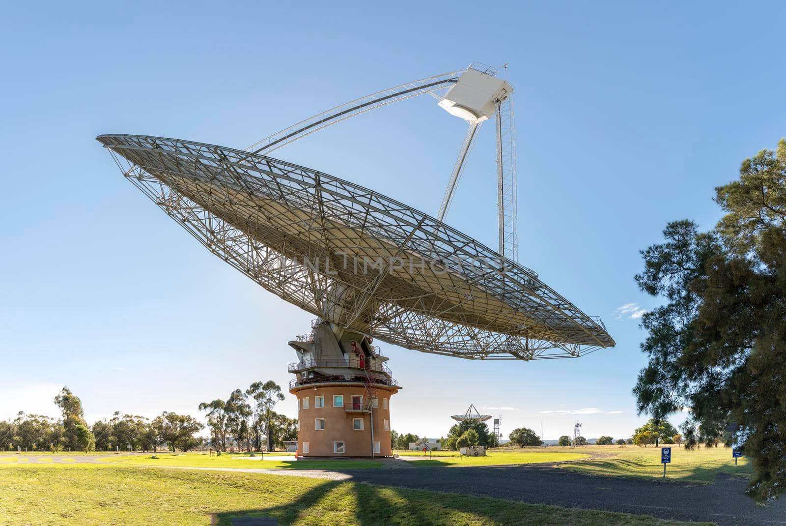 A large outdoor scientific radio telescope in the sunshine in a green field with trees