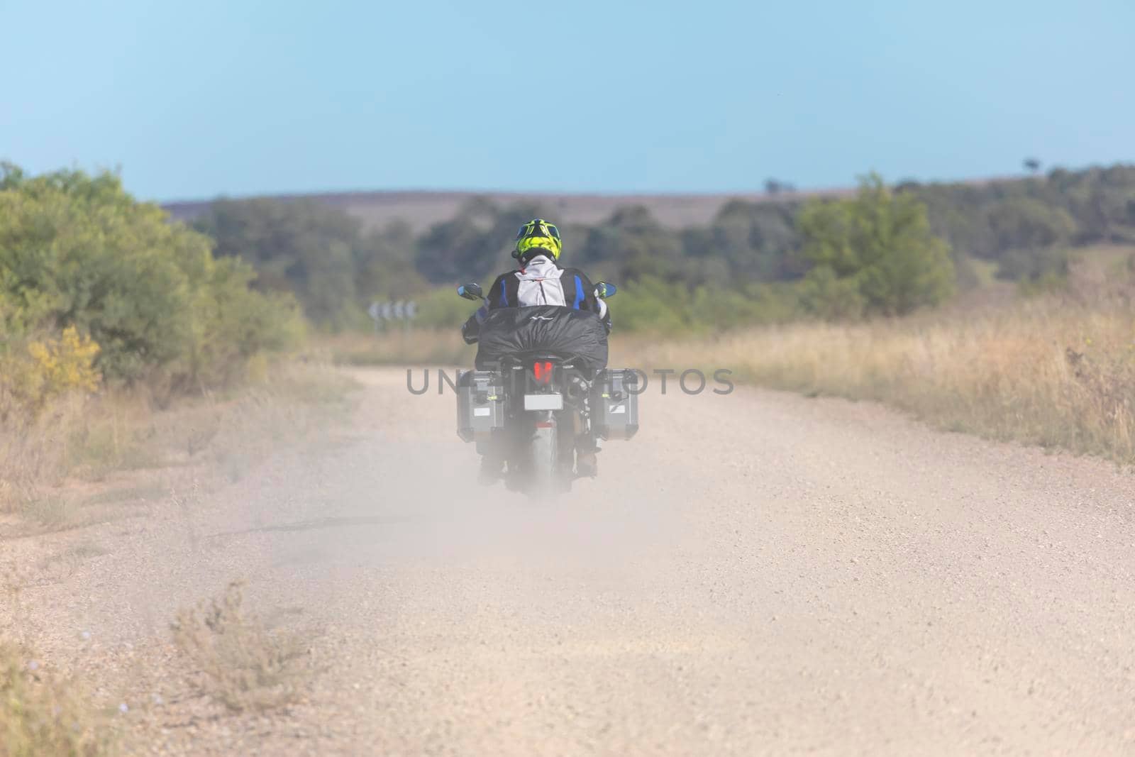 A person riding a motorcycle into the distance on a dusty dirty road