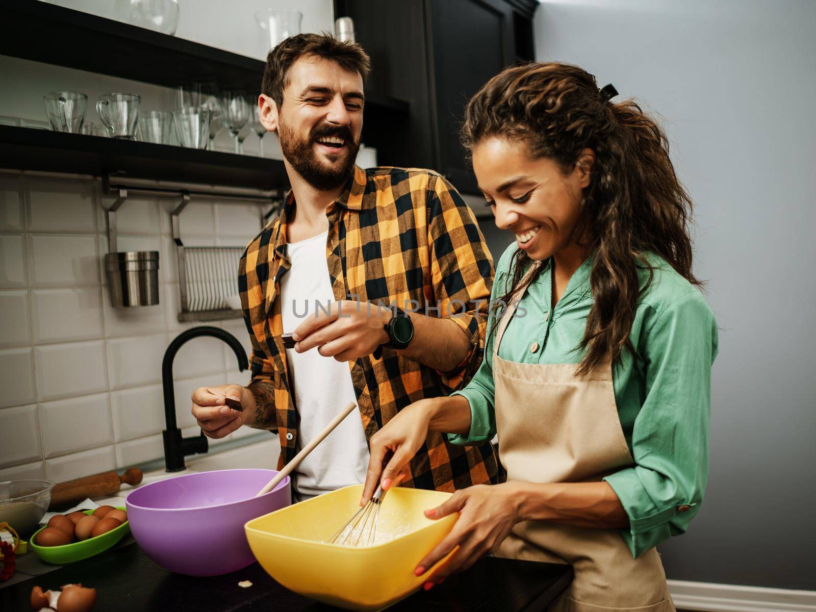 Happy multiracial couple cooking in their kitchen. They are making cookies and having fun.