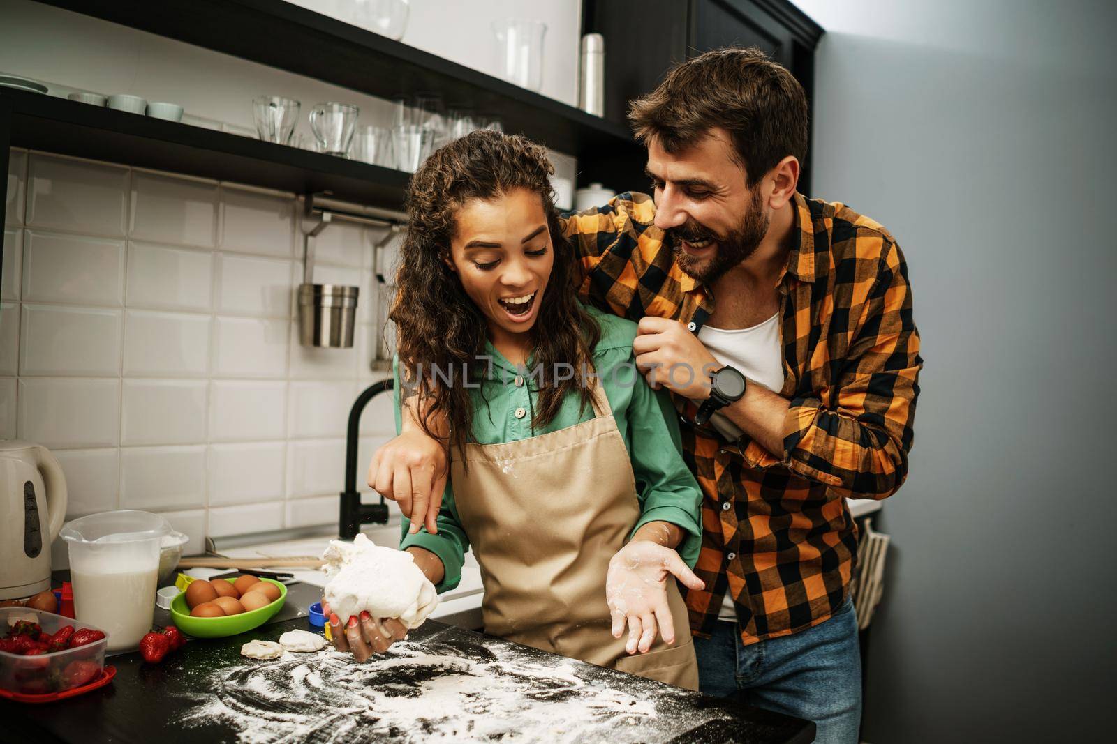 Happy multiracial couple cooking in their kitchen. They are making cookies.