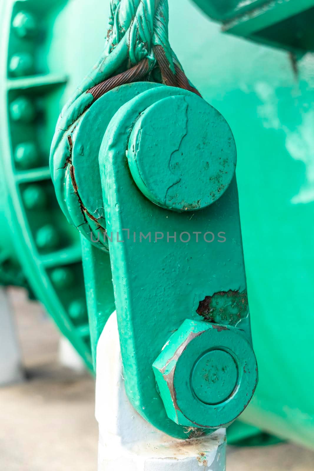 Close up view of of an old green steel shackle with a large nut and rusty steel cable