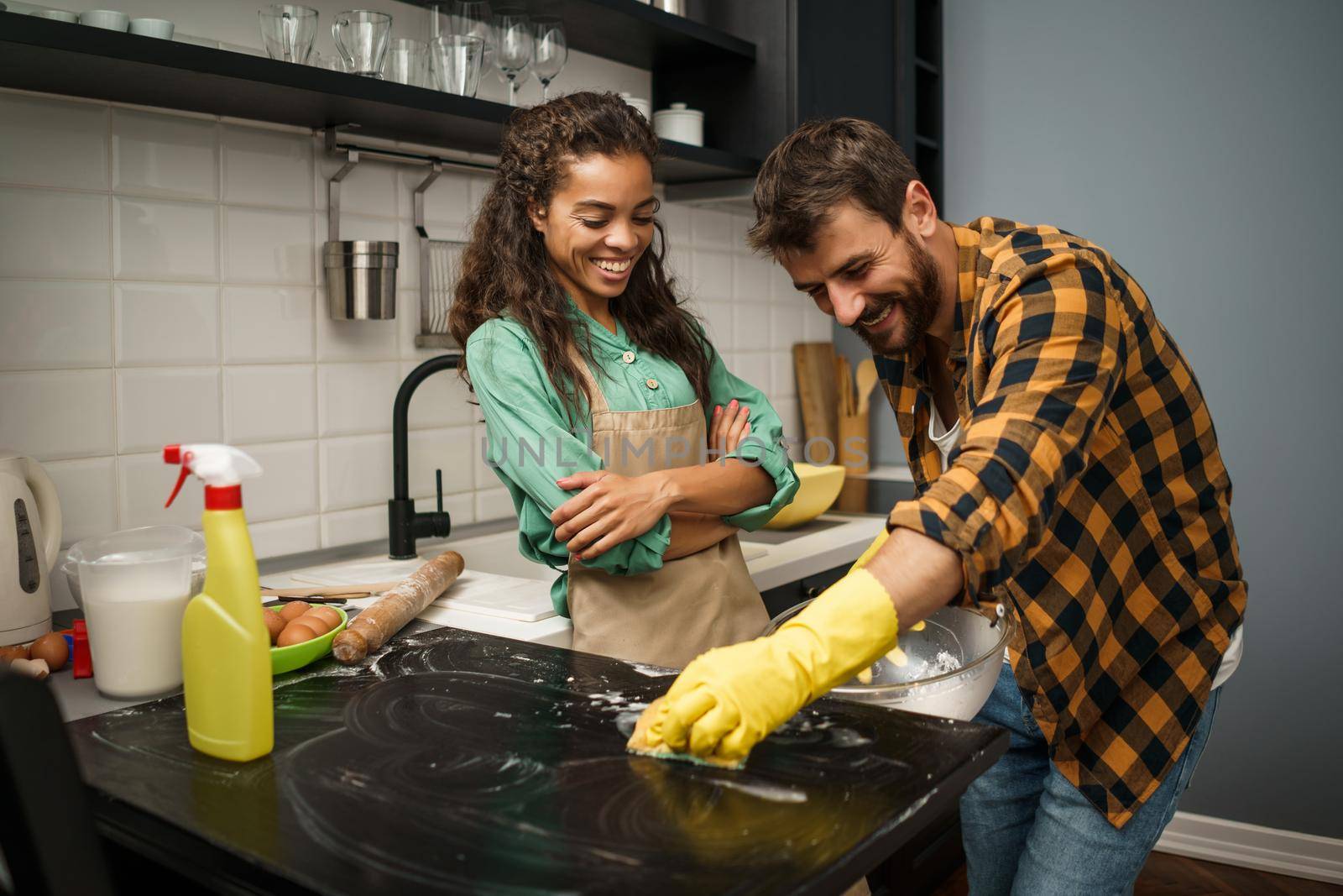 Happy multiracial couple is cleaning their kitchen and having fun.