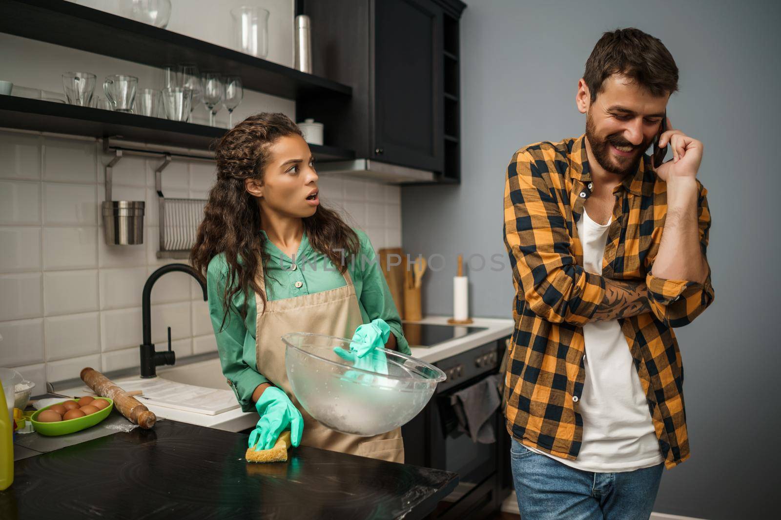 Young multiracial couple is cleaning their kitchen. They are arguing.