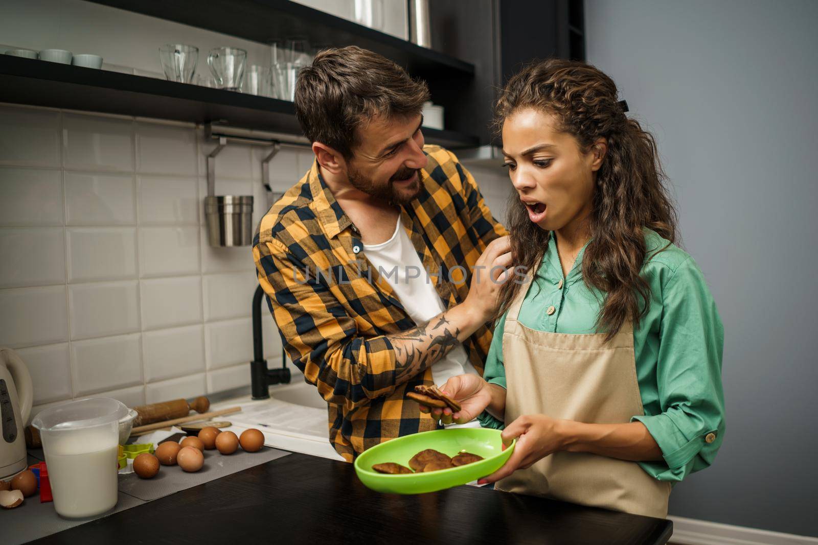 Multiracial couple is unhappy because cookies they have made are burnt.