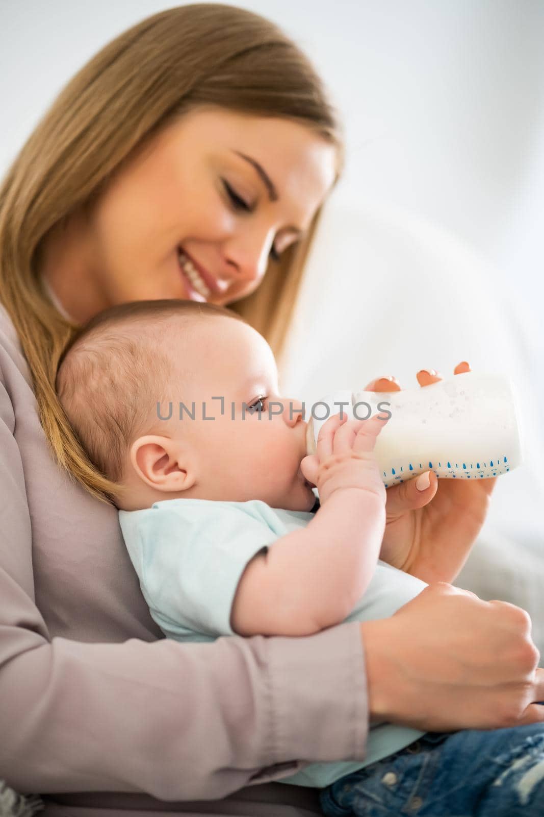 Happy mother is feeding her baby boy at home.