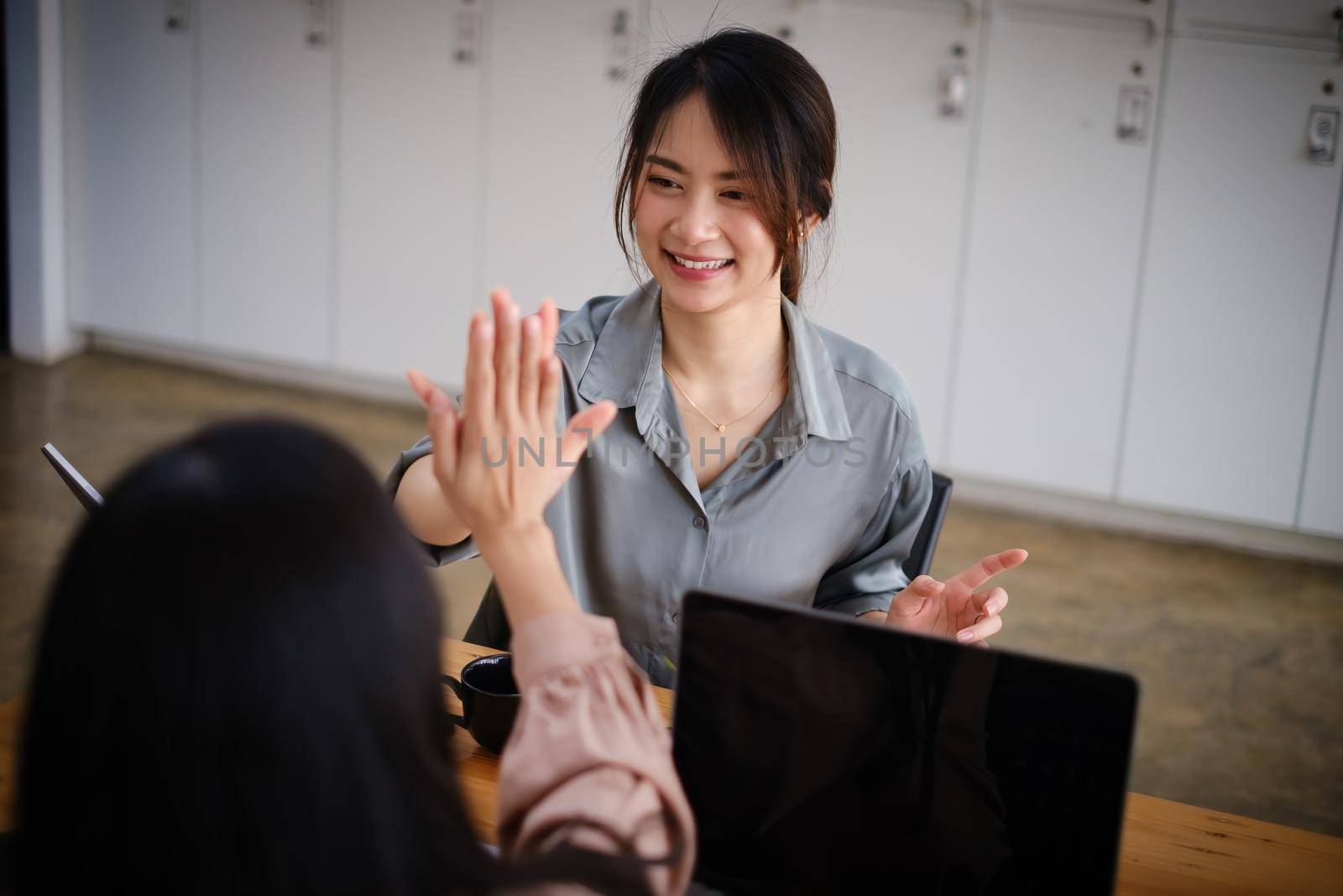 Business team giving a high fives gesture as they laugh and cheer their success. Achievement and Business Goal Success Concept. by itchaznong