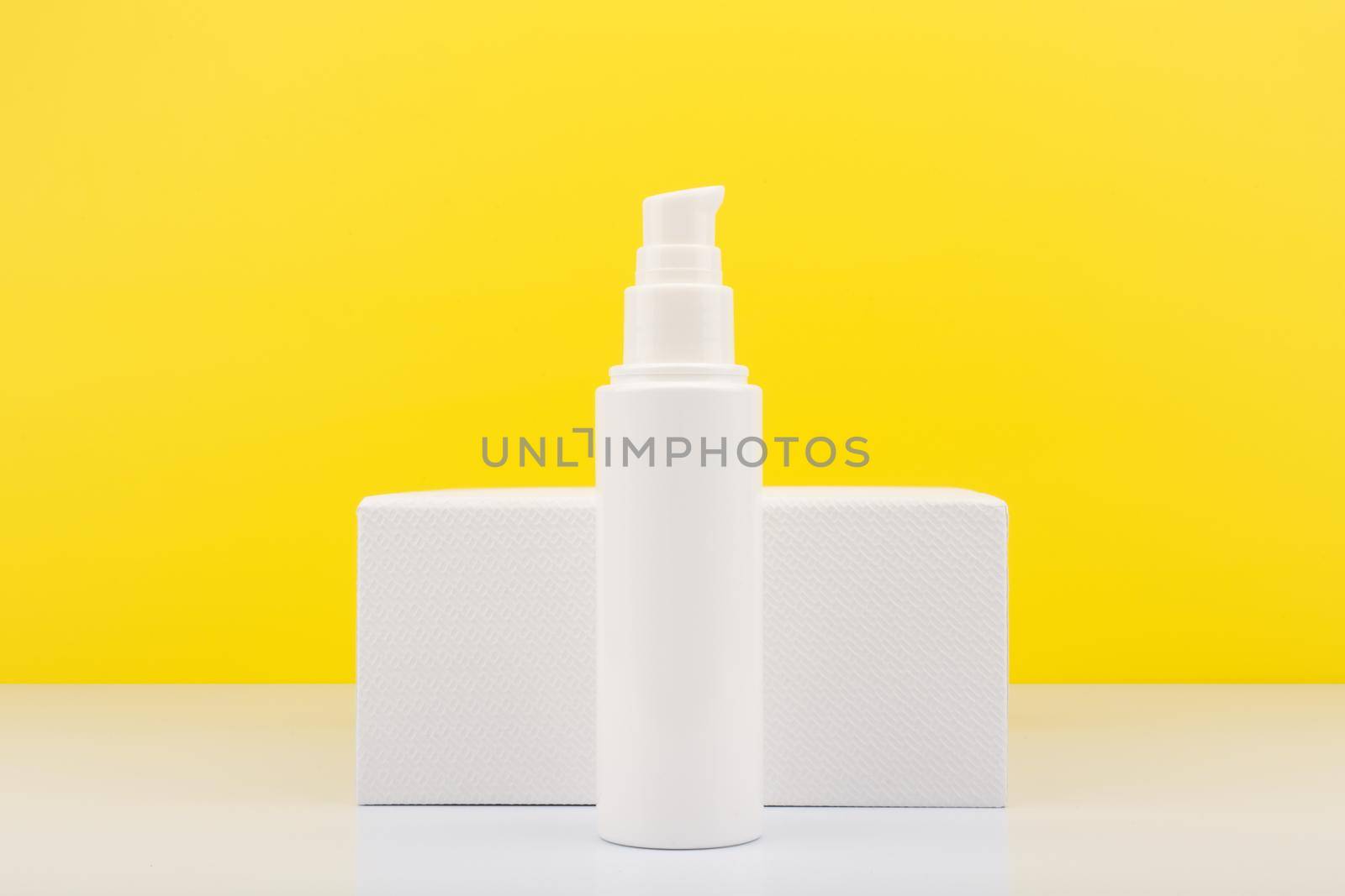 Face moisturizing cream or lotion in tall white tube against white geometric podium and yellow background with copy space. Concept of skin moisturizing and protective treatment with Spf for summer